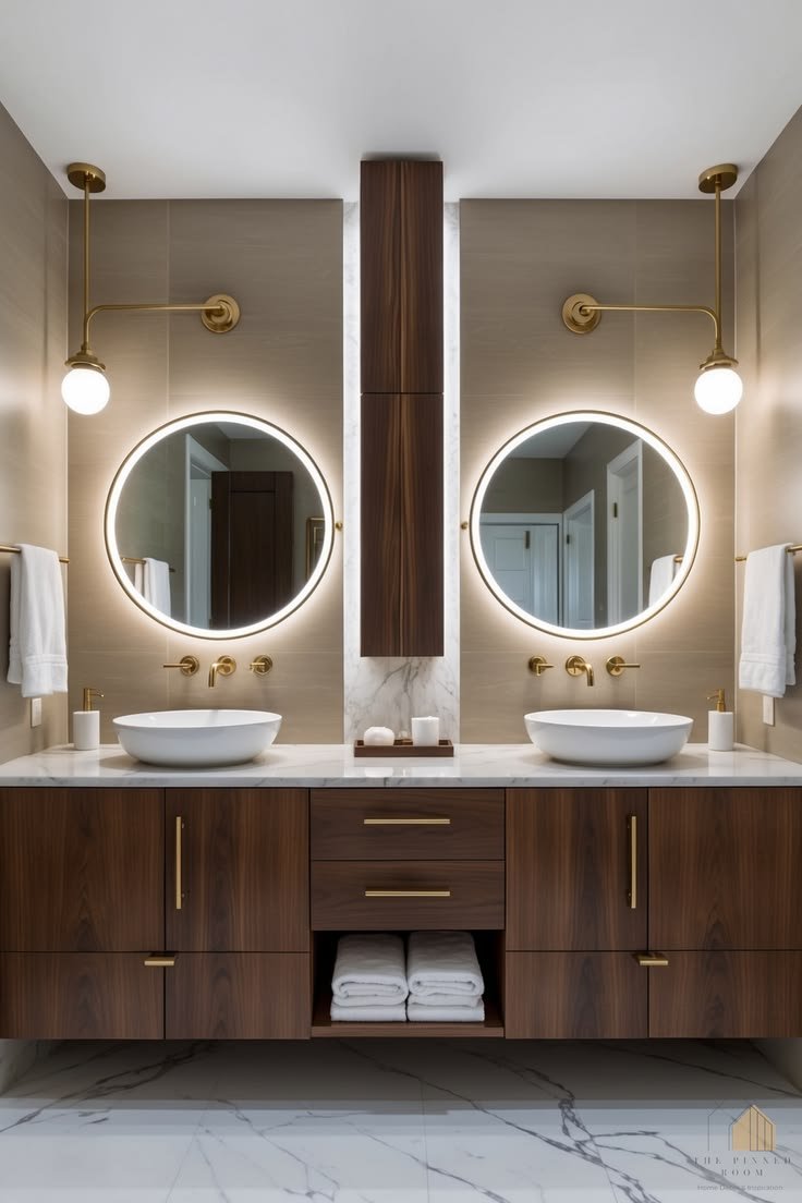 Double vanity bathroom with two round backlit mirrors, walnut cabinets and brass sconces
